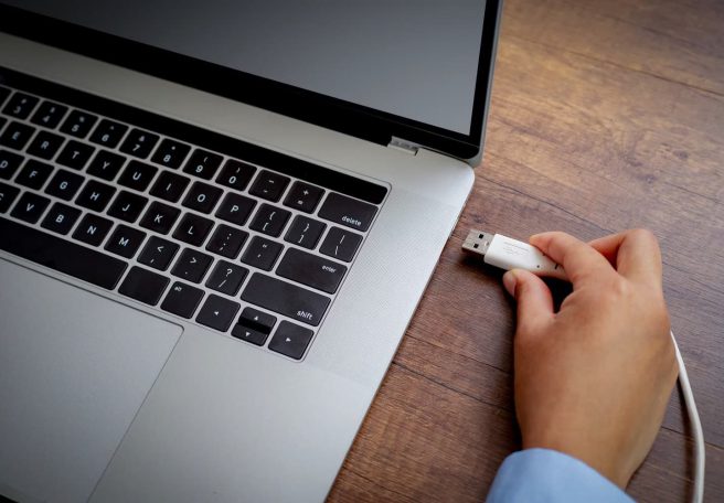 دستی در حال نگه داشتن کابل USB نزدیک پورت لپ‌تاپ
