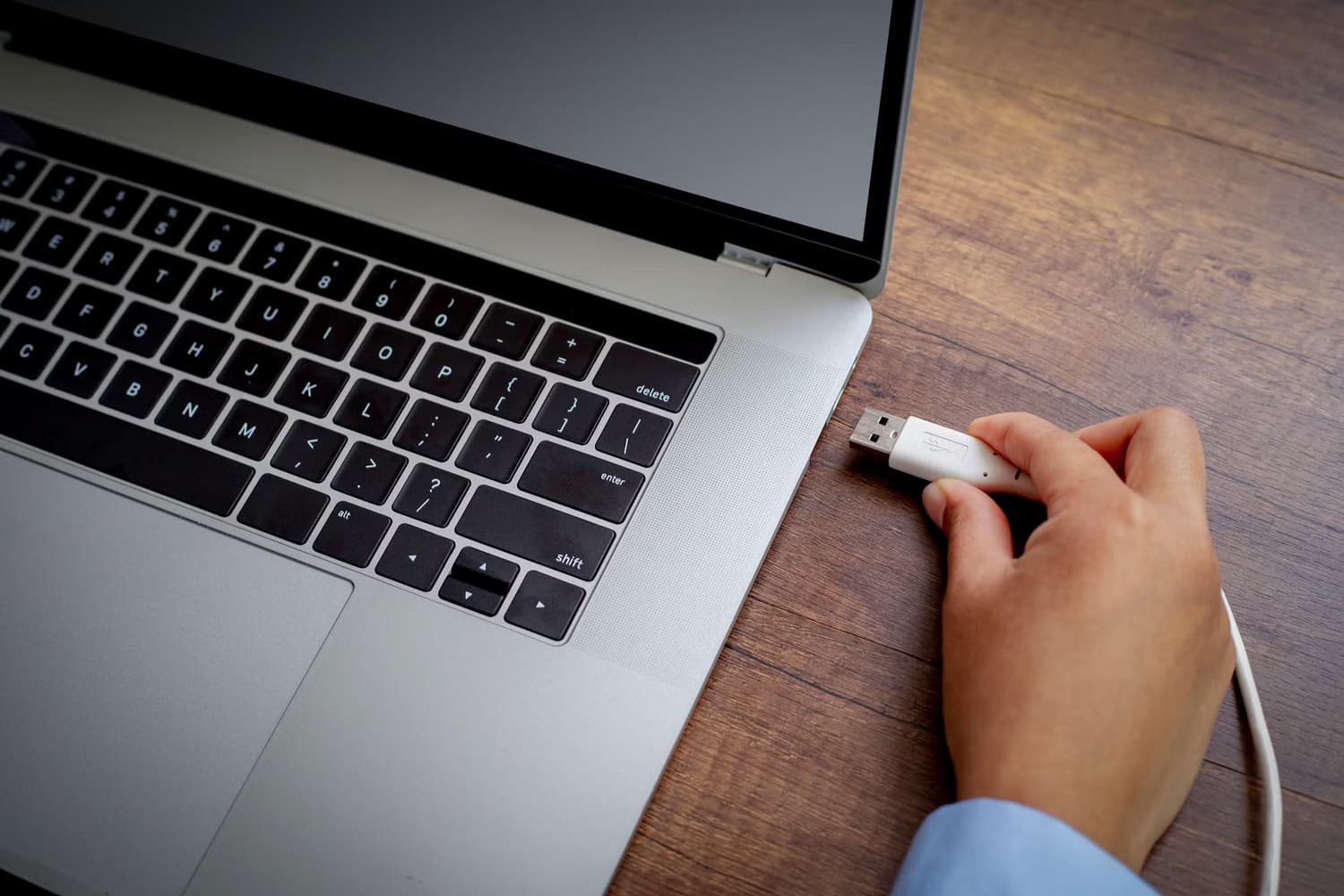 دستی در حال نگه داشتن کابل USB نزدیک پورت لپ‌تاپ